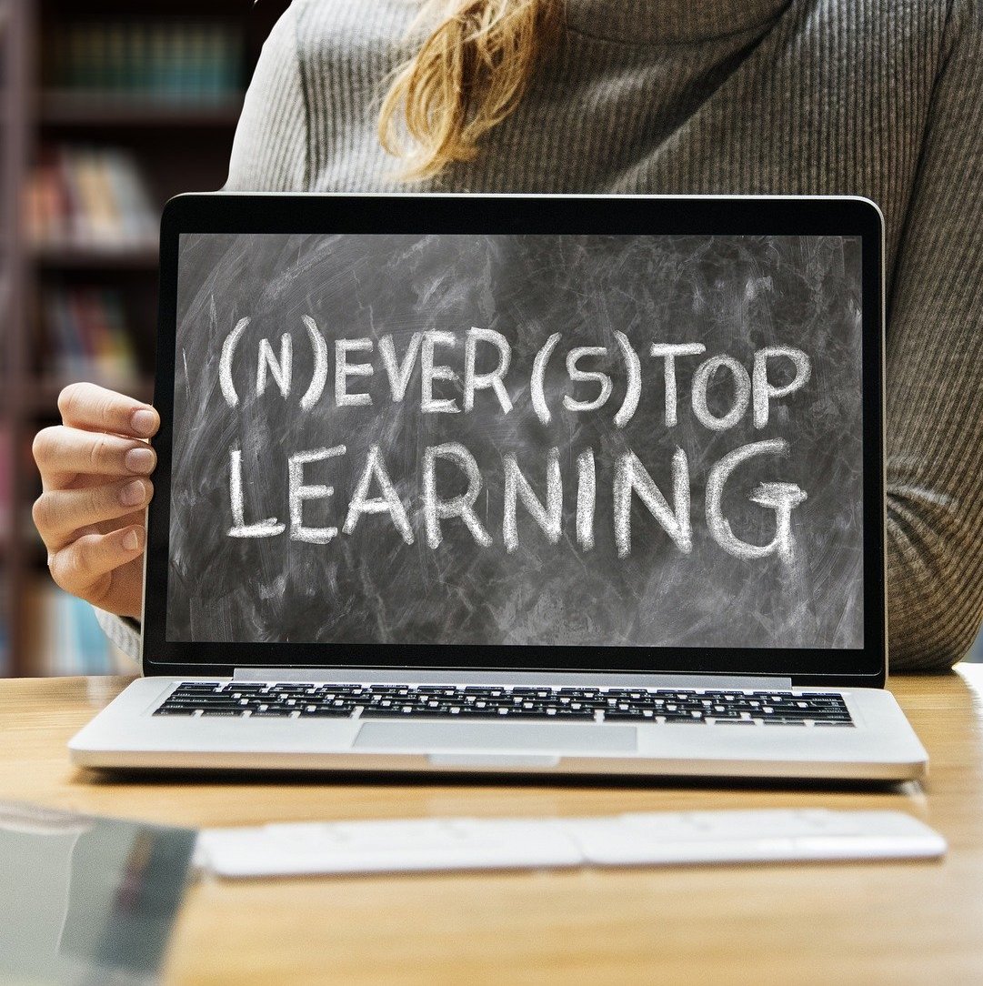 Woman's hand on laptop screen with the words Never Stop Learning