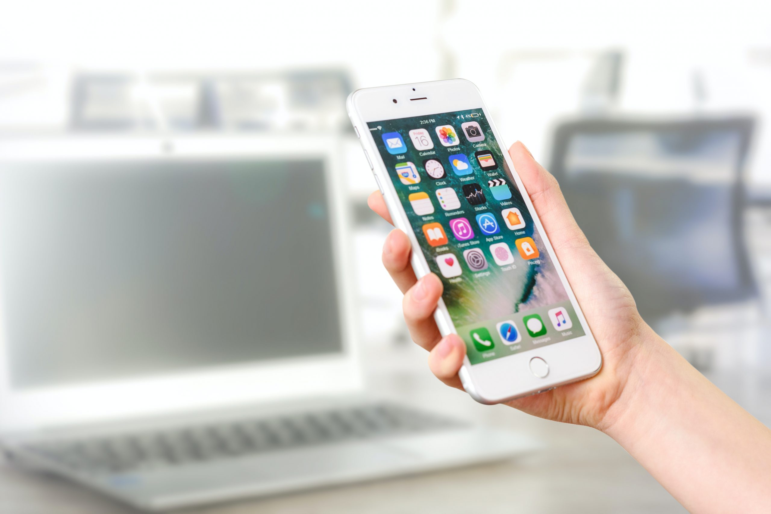 contact student services hand holding white iPhone with laptop in background